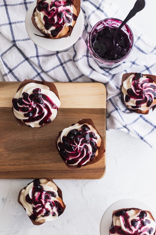 
Fluffy white cupcakes filled with blueberry preserves and topped with creme fraiche frosting, then a generous drizzle of blueberry sauce