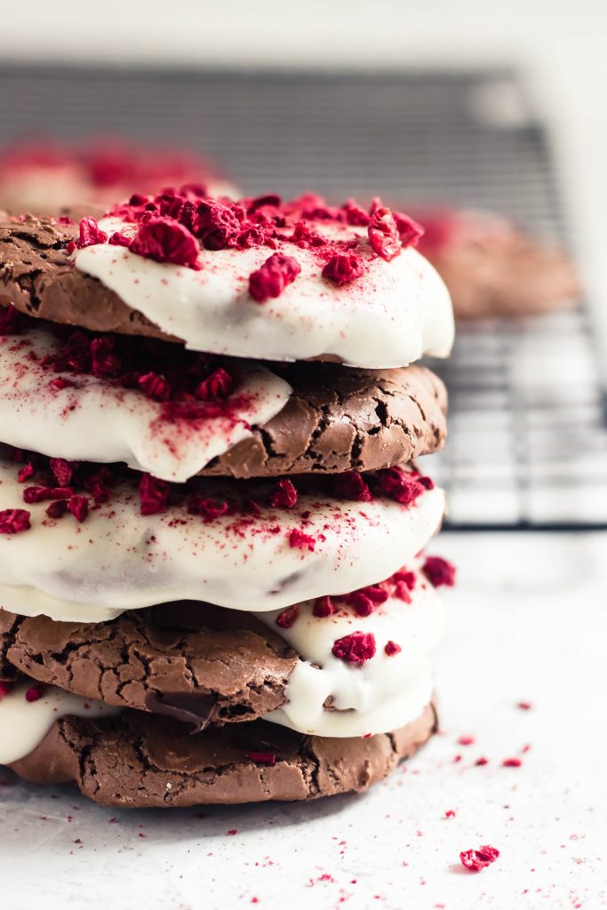 A stack of flourless chocolate cookies half dipped in white chocolate and sprinkled with crushed, bright red dried raspberry bits
