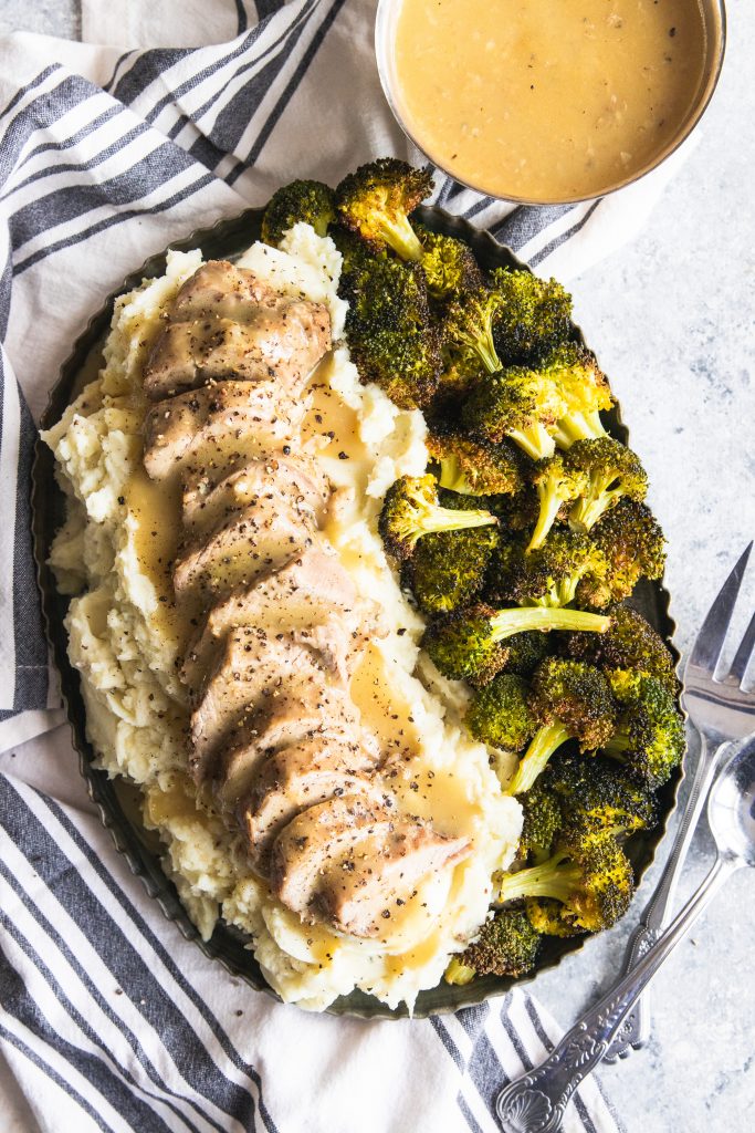 A platter of Dijon Pork Tenderloin piled on mashed potatoes and roasted broccoli on the side.