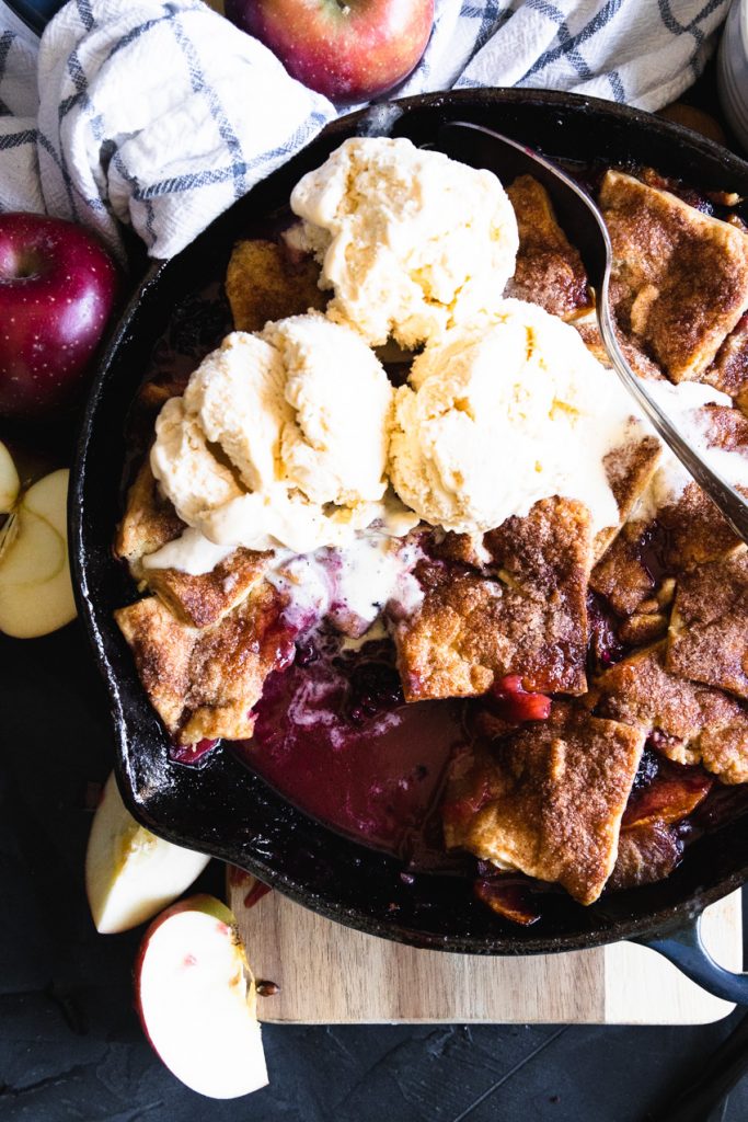 A pan of apple blackberry pandowdy with melty ice cream on top.