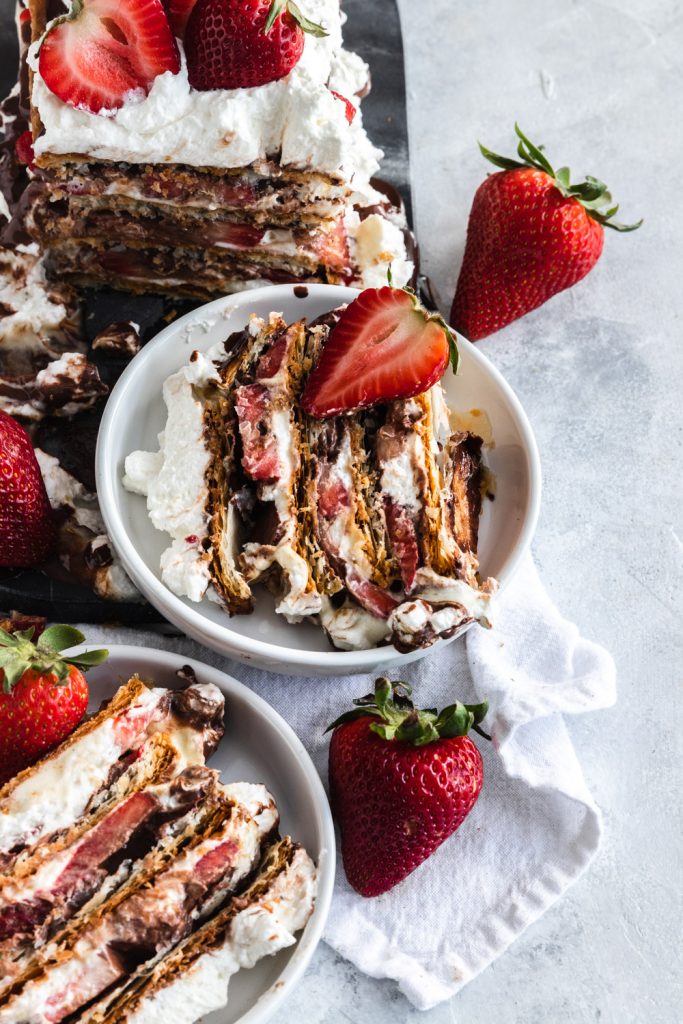 A slice of strawberry napoleon dessert with layers of puff pastry, pastry cream, whipping cream, fresh strawberries, and chocolate ganache.