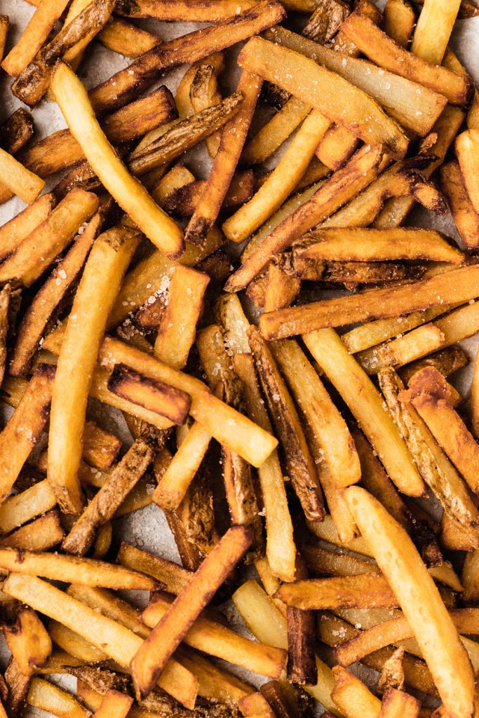 A tray of freshly fried homemade French fries, sprinkled with coarse sea salt.