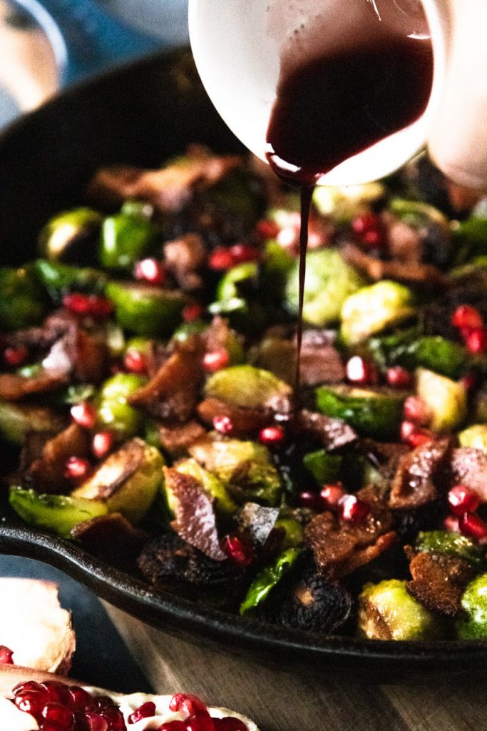 Pomegranate molasses being drizzled over pan seared brussels sprouts and bacon.
