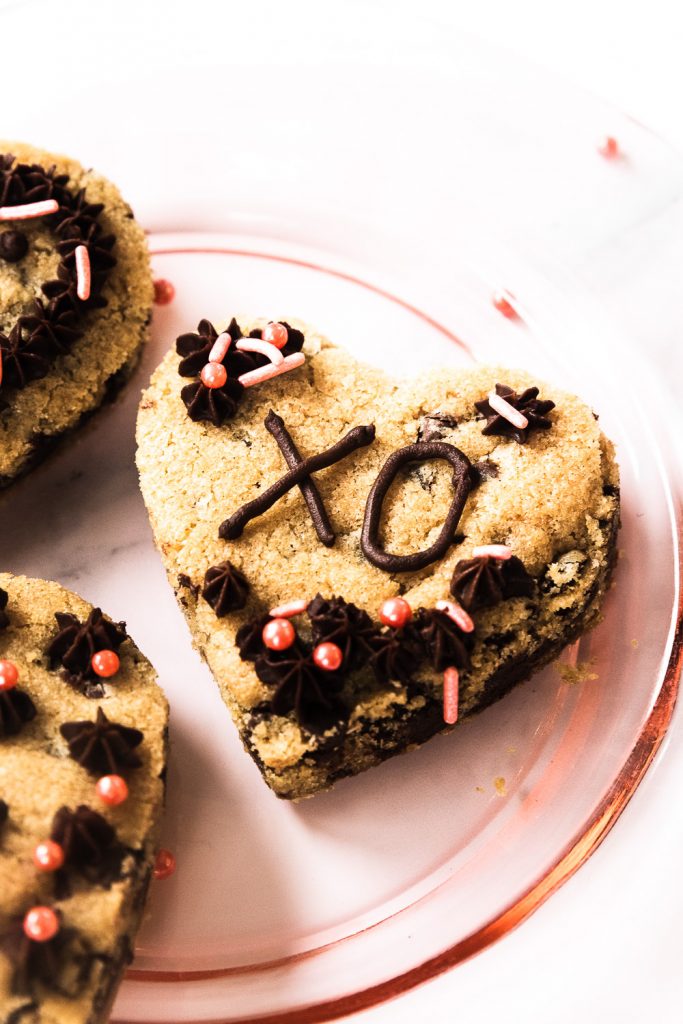 A sheet pan cookie cut into a heart and decorated with pink sprinkles and ganache to say "XO." 
