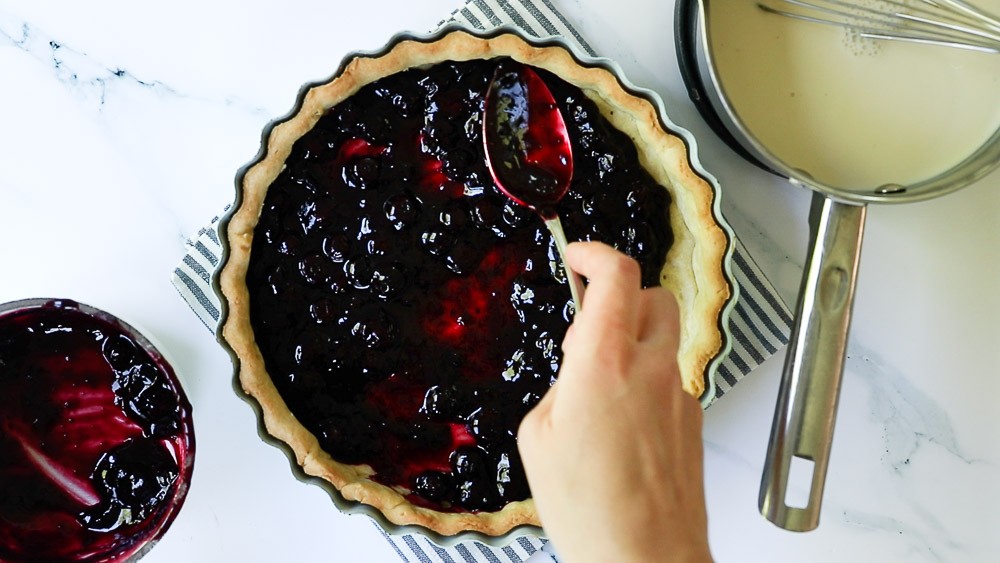 Spreading the cooked and cooled blueberry filling into the baked tart crust.