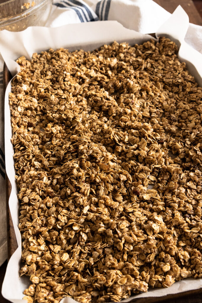 The granola spread out over a parchment lined baking sheet.
