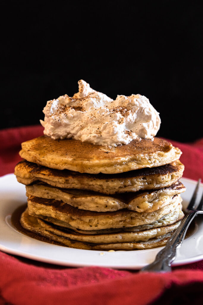 A stack of eggnog pancakes, topped with whipped cream and nutmeg.