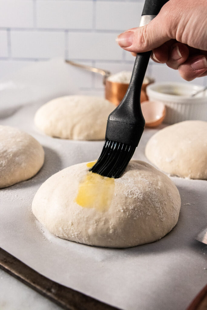 Adding egg wash to the top of each bread bowl with a pastry brush.