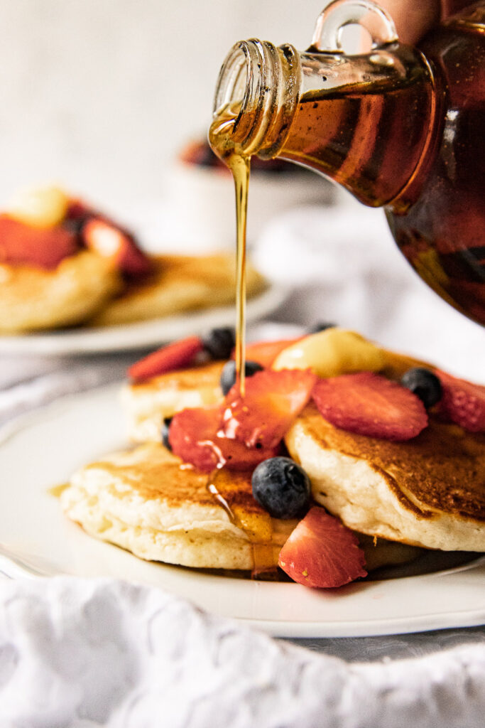 Pouring the vanilla bean maple syrup over a plate of pancakes.