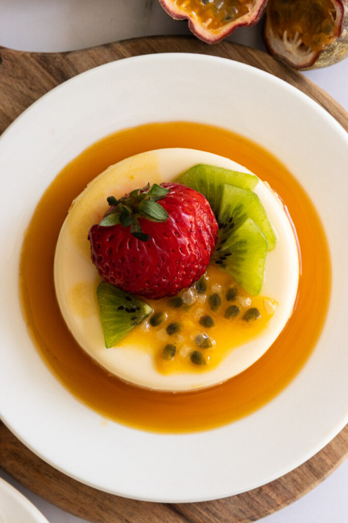 A passion fruit panna cotta on a plate, topped with strawberry, passion fruit, and kiwi.