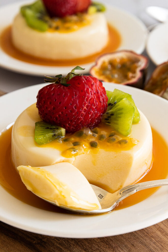 A passion fruit panna cotta on a plate, topped with strawberry, passion fruit, and kiwi.