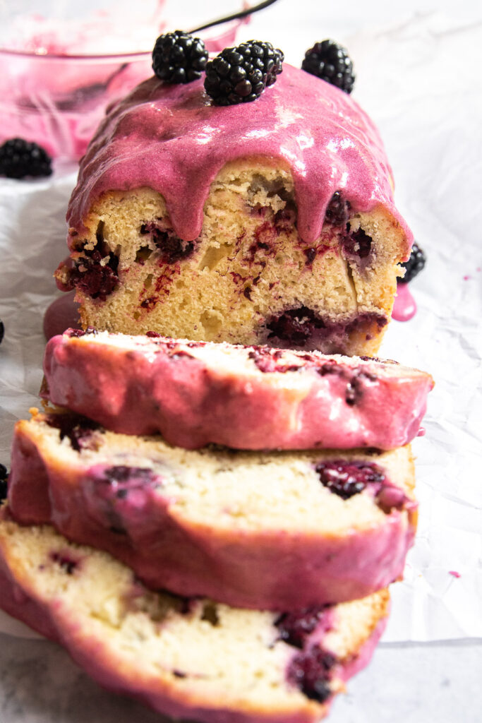 A sliced blackberry loaf cake with blackberry glaze dripping down.