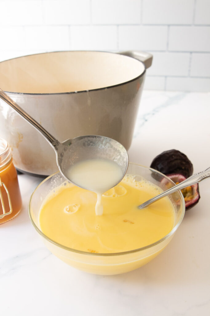 Whisking some of the hot cream and milk into the egg yolks.