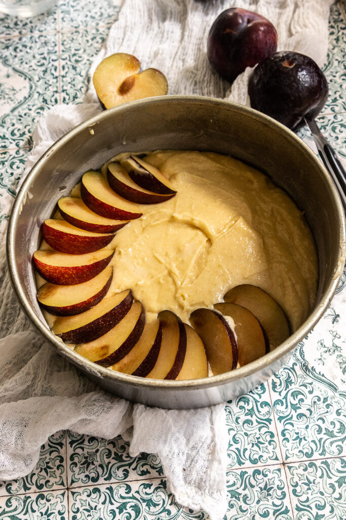 Layer the sliced plums on top of the cake in the cake tin.