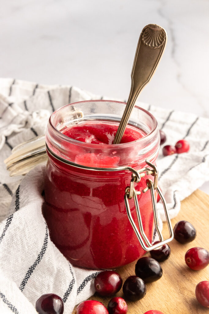 A jar of cranberry curd with a spoon in it.