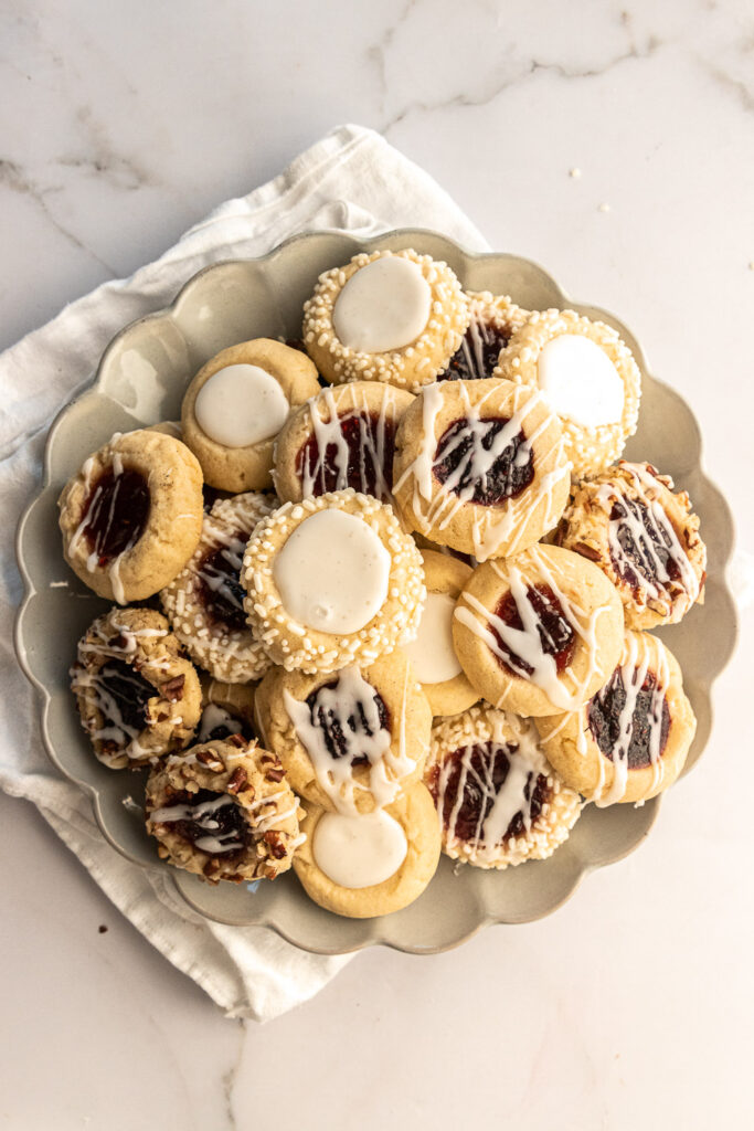A plate full of thumbprint cookies, some filled with icing and some filled with jam.