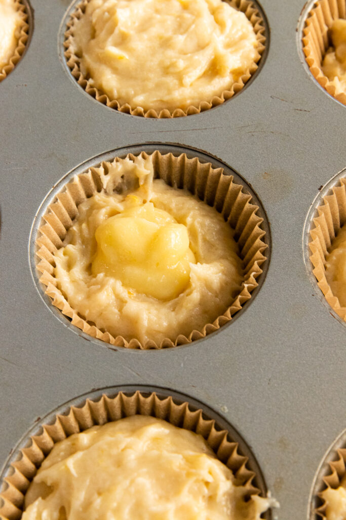 A muffin tin, half full of batter, and topped with lemon curd.
