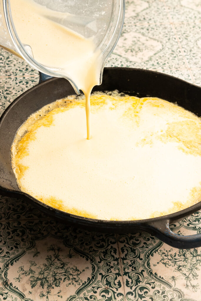 Pouring the dutch baby batter into the hot skillet.