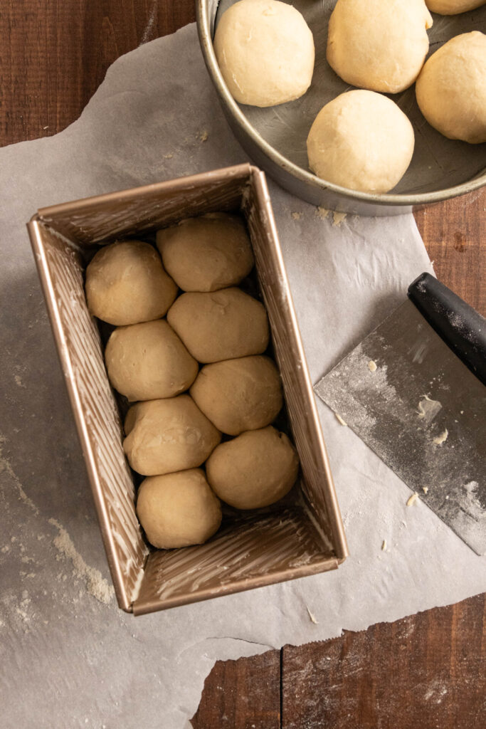 Placing the shaped balls of dough into the buttered loaf pans.