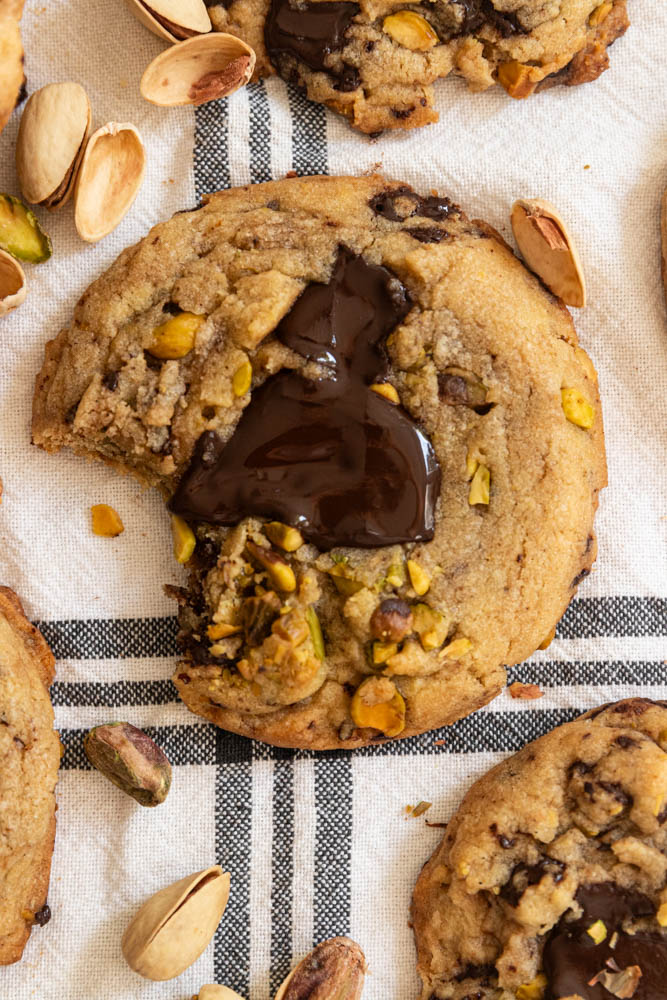 A cookie with pistachios and melty chocolate on top. A bite is taken out of the cookie.