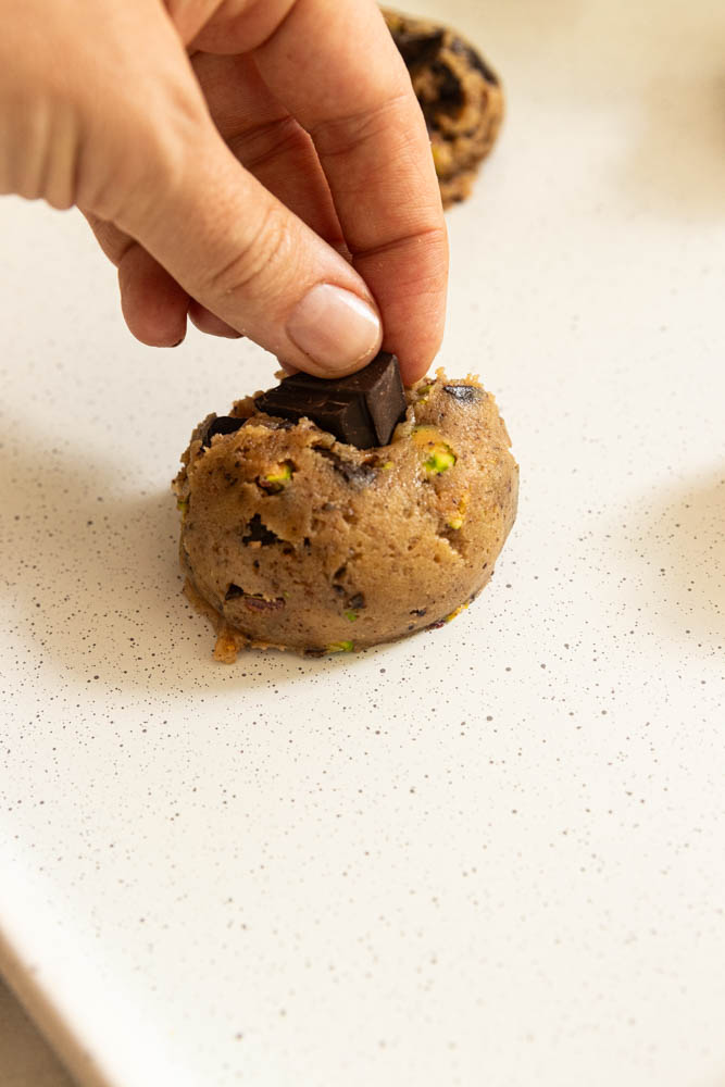 Pressing a chunk of chocolate into the top of a ball of cookie dough.