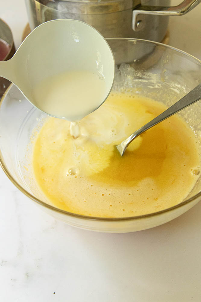 Slowly drizzle the heated milk and cream into the egg yolk  mixture to gradually warm it.