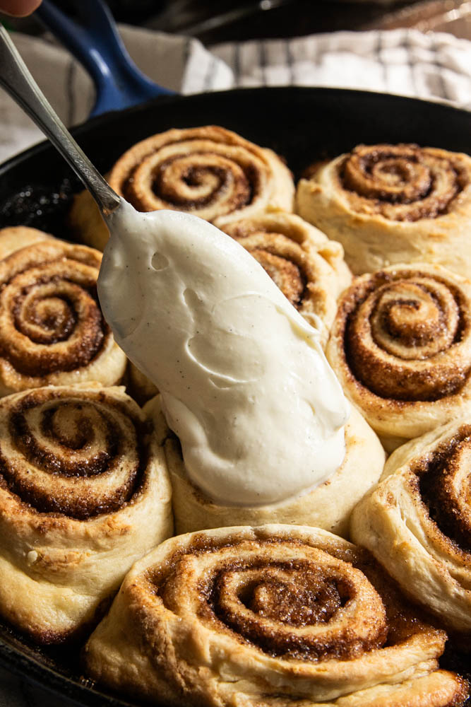 Spreading the frosting over the top of the warm rolls.