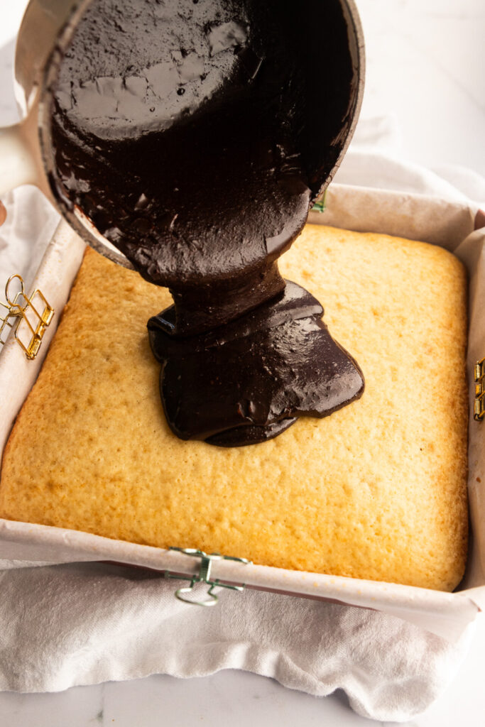 Pouring cooked chocolate frosting over the sourdough vanilla cake.