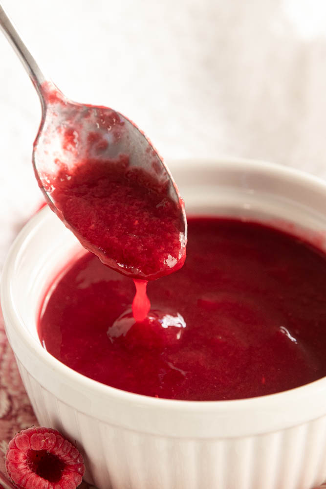 Raspberry coulis sauce, dripping of of a spoon.