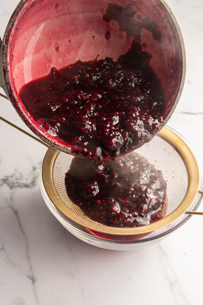 Pouring the coulis through a strainer into a bowl.