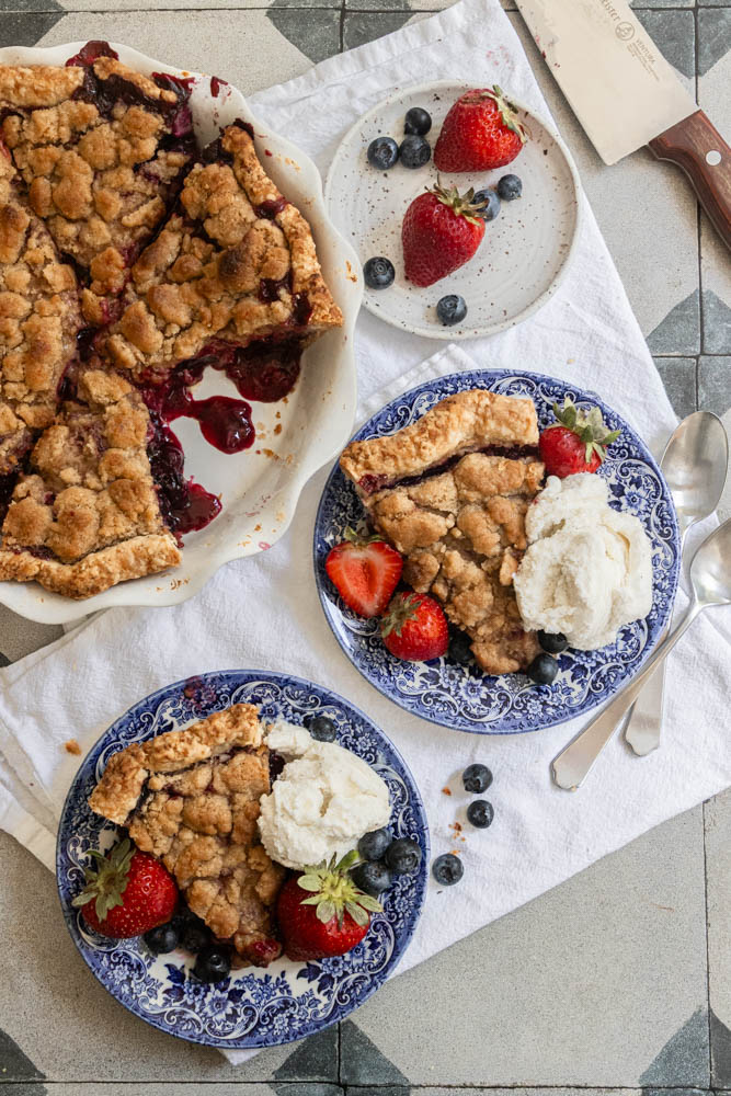 Slices of Strawberry Blueberry Pie with a crumble topping and vanilla ice cream on the side.