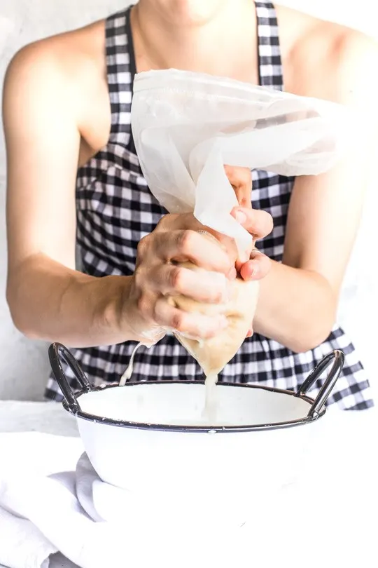A recipe of freshly made peanut milk being squeezed through a nut bag.