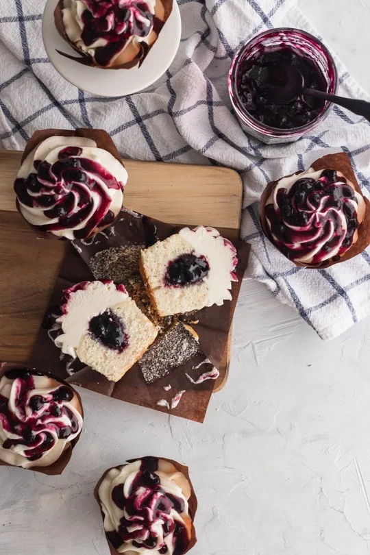 Fluffy white cupcakes filled with blueberry preserves and topped with creme fraiche frosting, then a generous drizzle of blueberry sauce