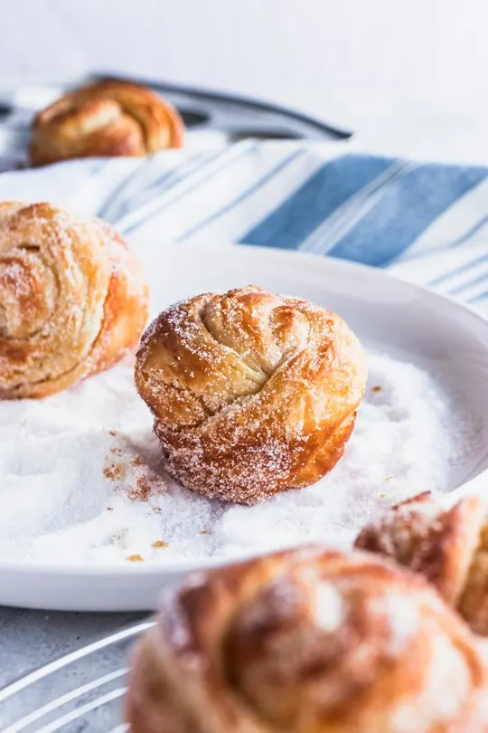 Warm, flaky cruffins (croissants and muffins in one) being rolled in sugar.