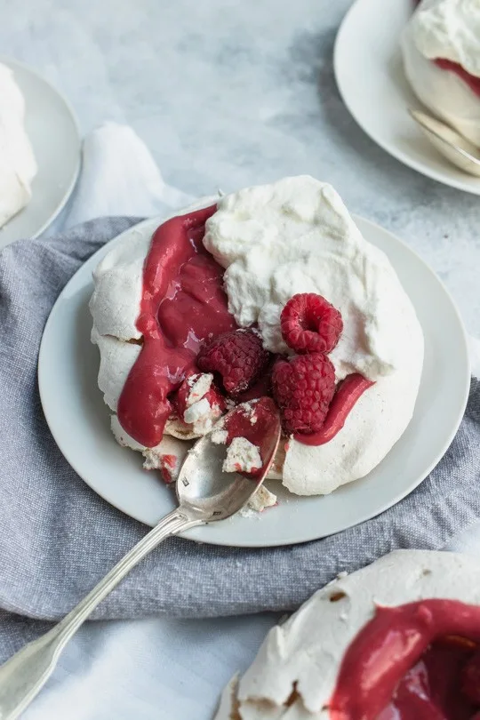 A spoon shattering a mini pavlova with Raspberry Curd and Whipped Cream