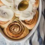 A pan of perfectly swirled cinnamon rolls with fluffy white frosting being spread over them.