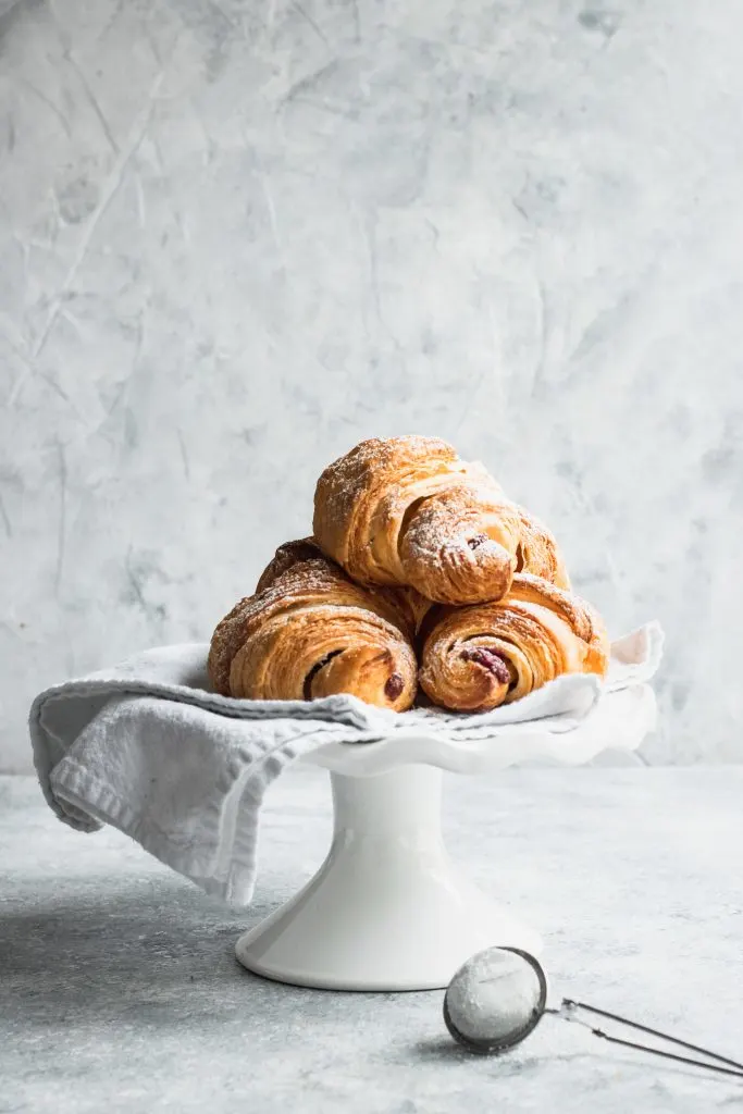 Piled on a white plate, these flaky croissants are filled with Chocolate and Raspberry Filling and dusted with powdered sugar.