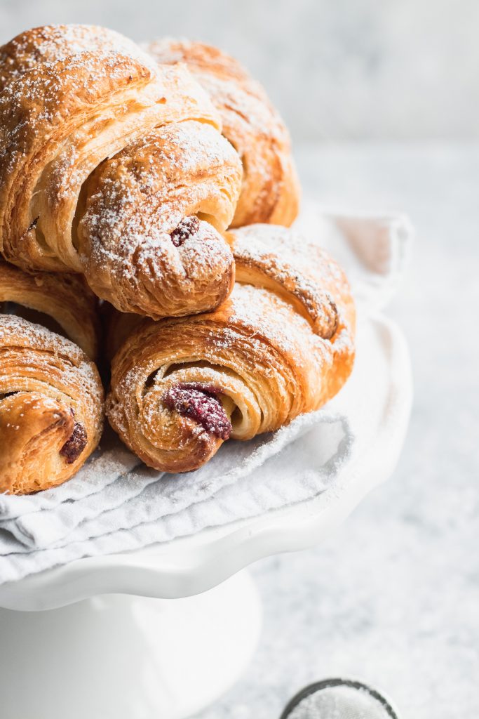 Piled on a white plate, these flaky croissants are filled with Chocolate and Raspberry Filling and dusted with powdered sugar.