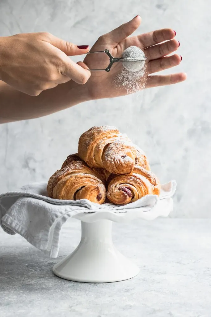 Piled on a white plate, these flaky croissants are filled with Chocolate and Raspberry Filling and being dusted with powdered sugar.