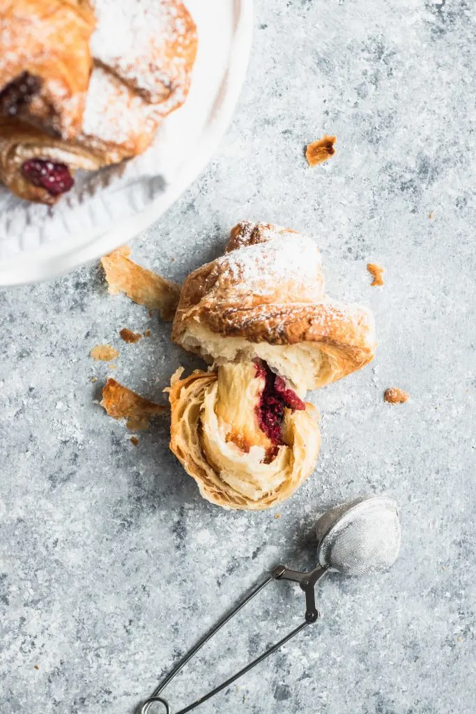 A flaky croissant torn in half to show the raspberry and chocolate filling.