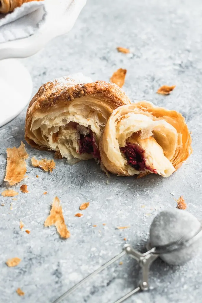 A flaky croissant torn in half to show the raspberry and chocolate filling.