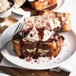 Peppermint Bark French Toast is stuffed with a cream cheese filling, then piled high with whipped cream, peppermint bark, and drizzled with chocolate ganache