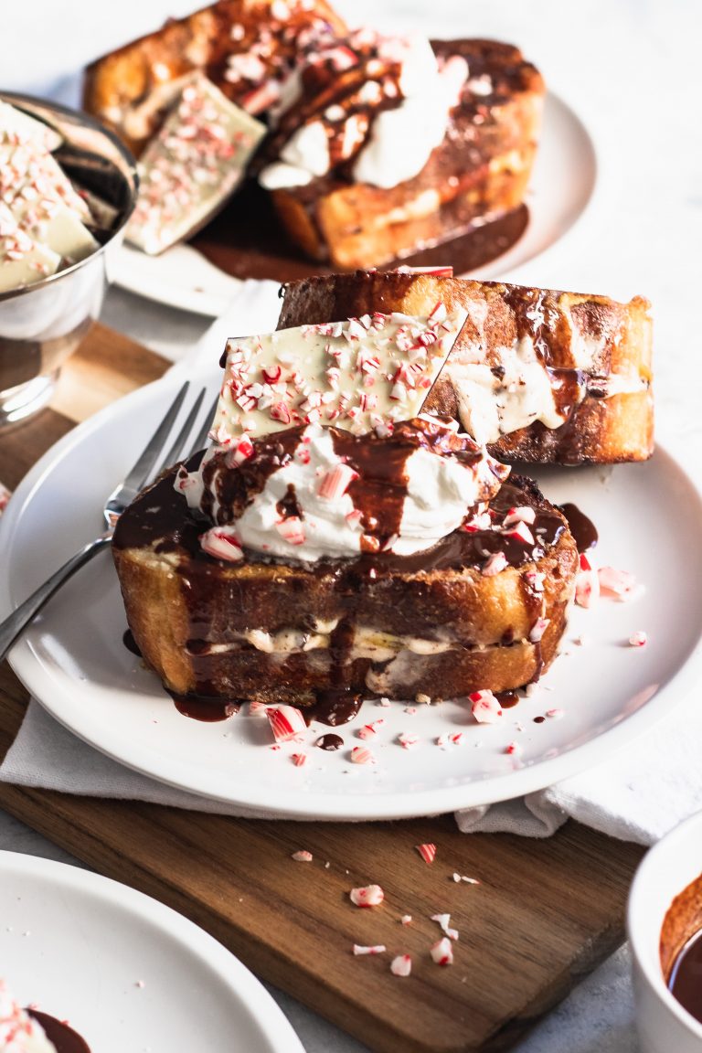 Peppermint Bark French Toast is stuffed with a cream cheese filling, then piled high with whipped cream, peppermint bark, and drizzled with chocolate ganache