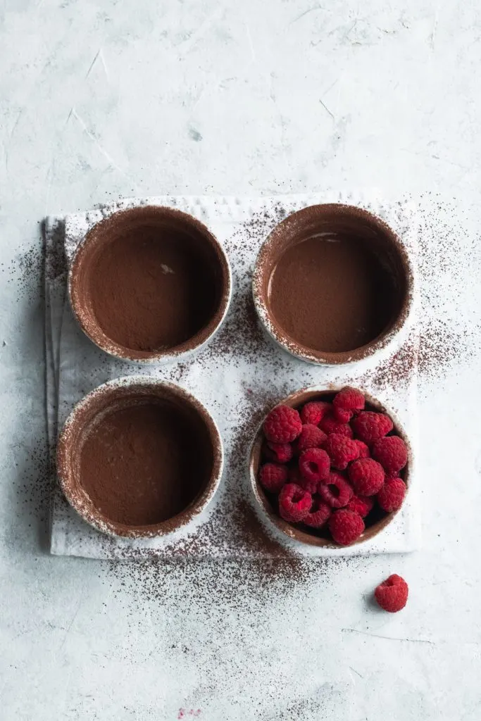 Ramekins dusted with cocoa powder and one filled with raspberries