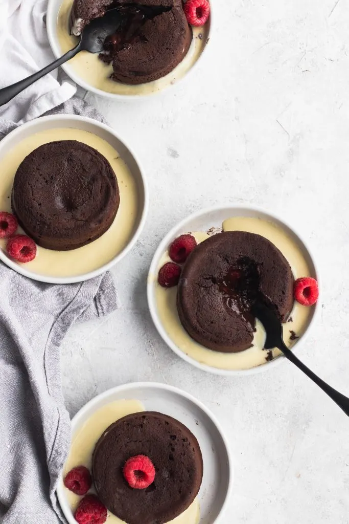 Raspberry Chocolate Lava Cakes with an oozing chocolate and raspberry center, garnished with creme anglaise and fresh raspberries