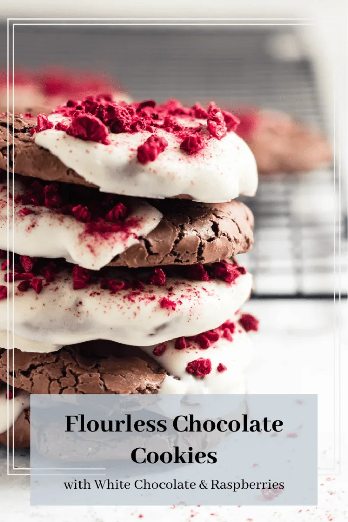 A stack of flourless chocolate cookies half dipped in white chocolate and sprinkled with crushed, bright red dried raspberry bits