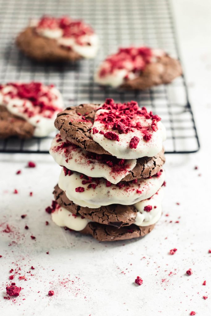 A stack of flourless chocolate cookies half dipped in white chocolate and sprinkled with crushed, bright red dried raspberry bits