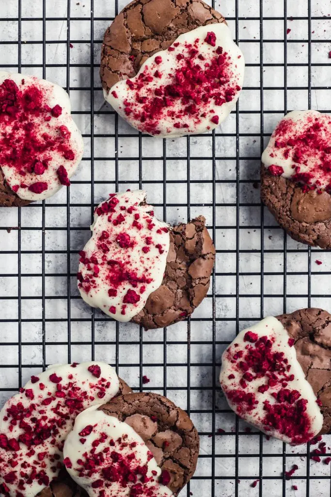 A stack of flourless chocolate cookies half dipped in white chocolate and sprinkled with crushed, bright red dried raspberry bits