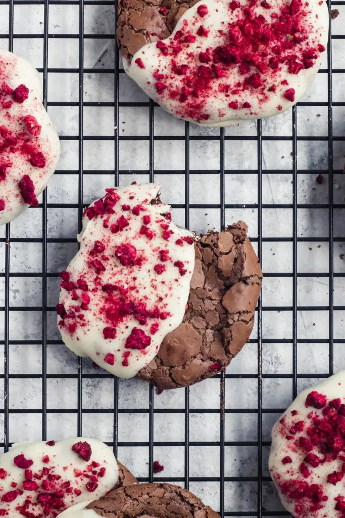 A stack of flourless chocolate cookies half dipped in white chocolate and sprinkled with crushed, bright red dried raspberry bits