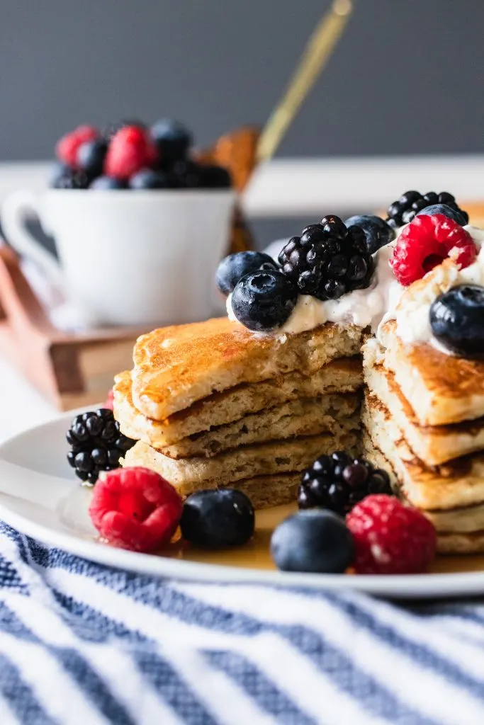 A stack of overnight sourdough pancakes, topped with whipping cream and berries, then with a drizzle of maple syrup.